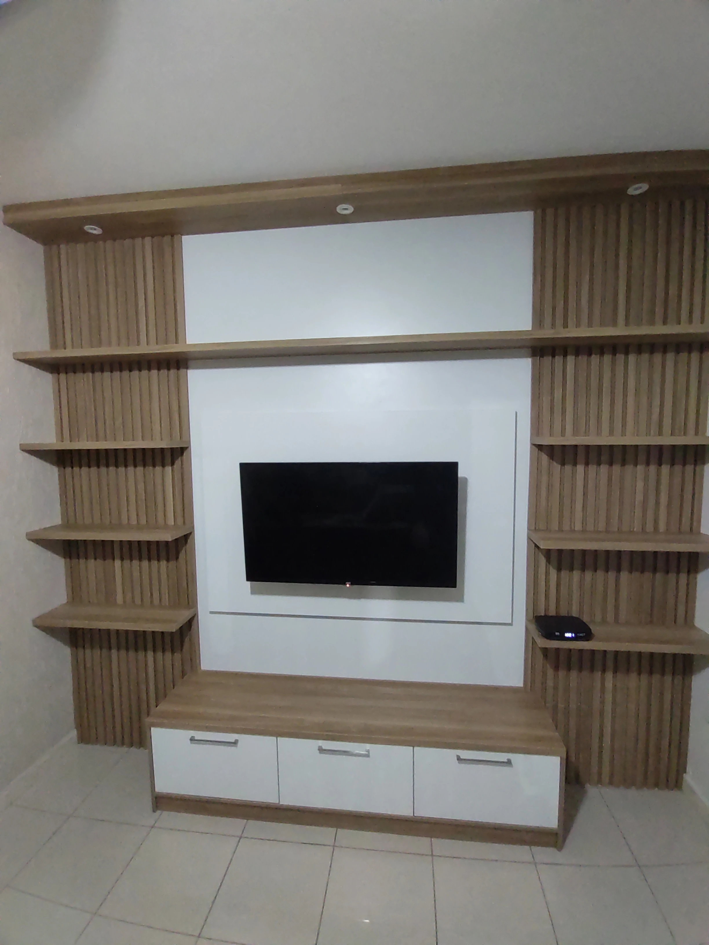 Painel de sala branco com uma televisão no meio e ripado amadeirado nas laterais, com prateleiras e um rack no meio com duas portas